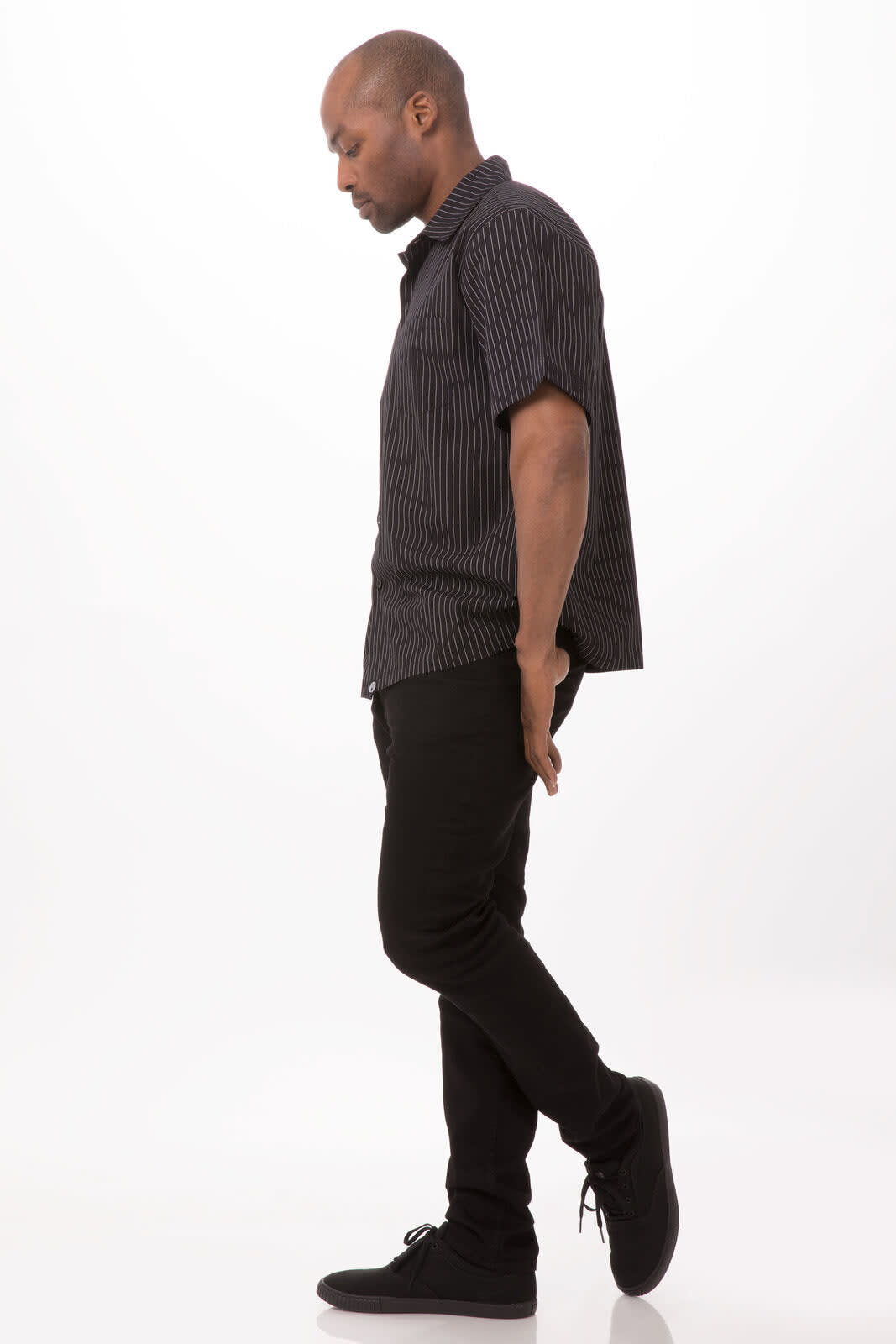 A chef shirt in black with vertical stripes, paired with black pants and dark shoes, on a model standing sideways.