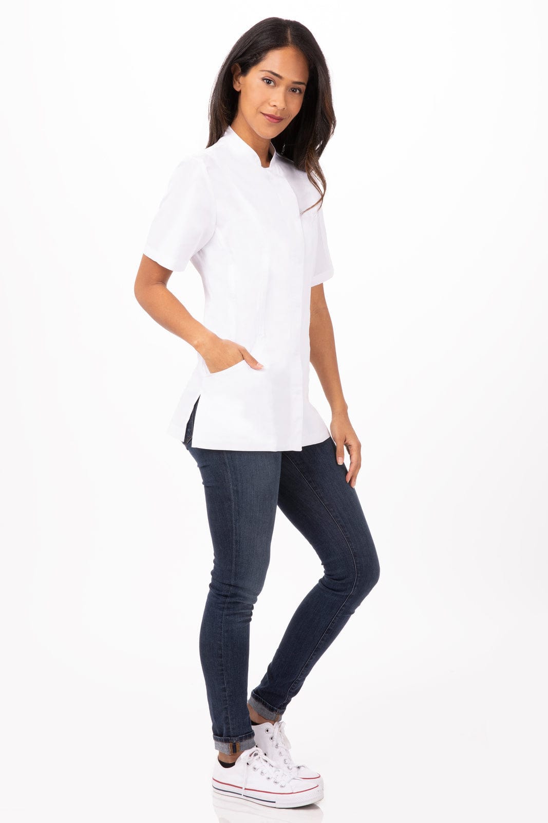 A woman wearing a white chef jacket with short sleeves, paired with dark jeans and sneakers. The jacket has a logo.