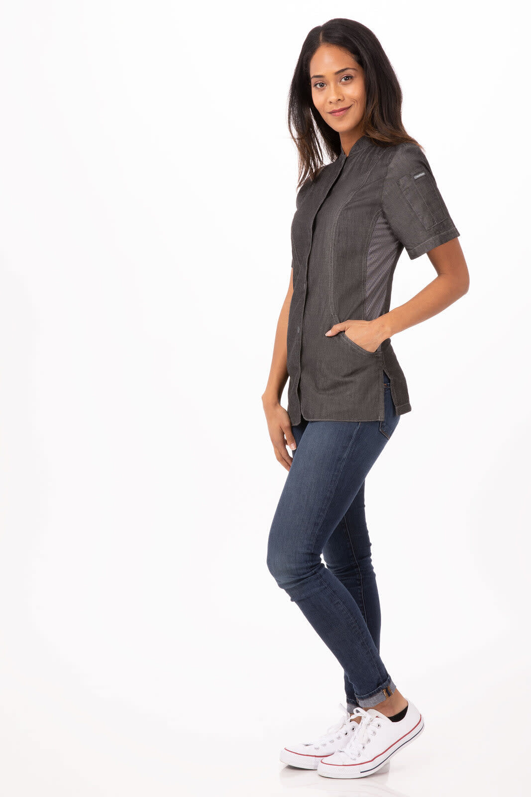 A women's chef jacket in charcoal grey, featuring short sleeves and pockets, paired with jeans and sneakers.