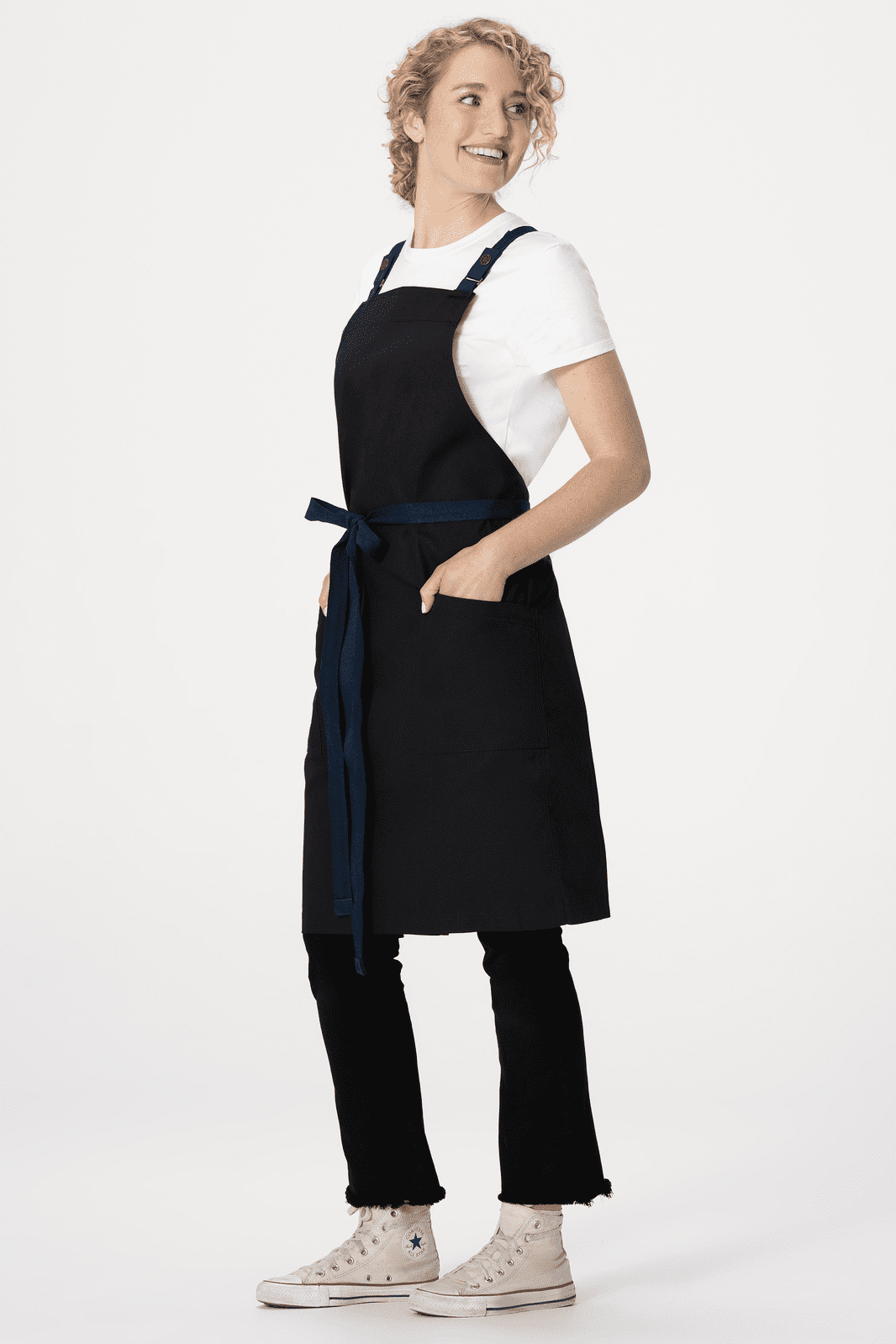 A black cross back apron with a blue tie, worn over a white shirt and black pants, featuring pockets.