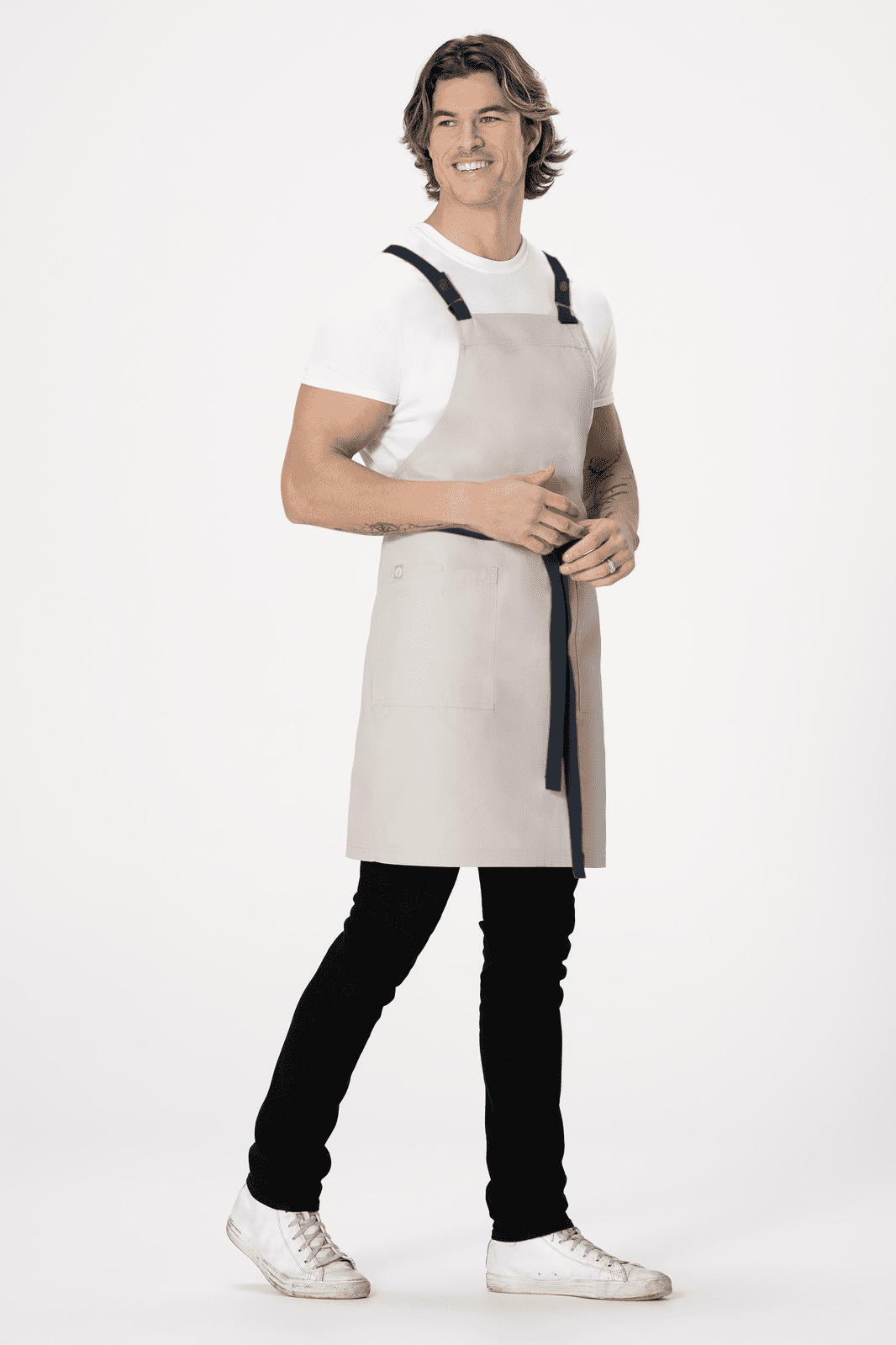 A man wearing a grey cross back apron with black straps, standing against a plain background.