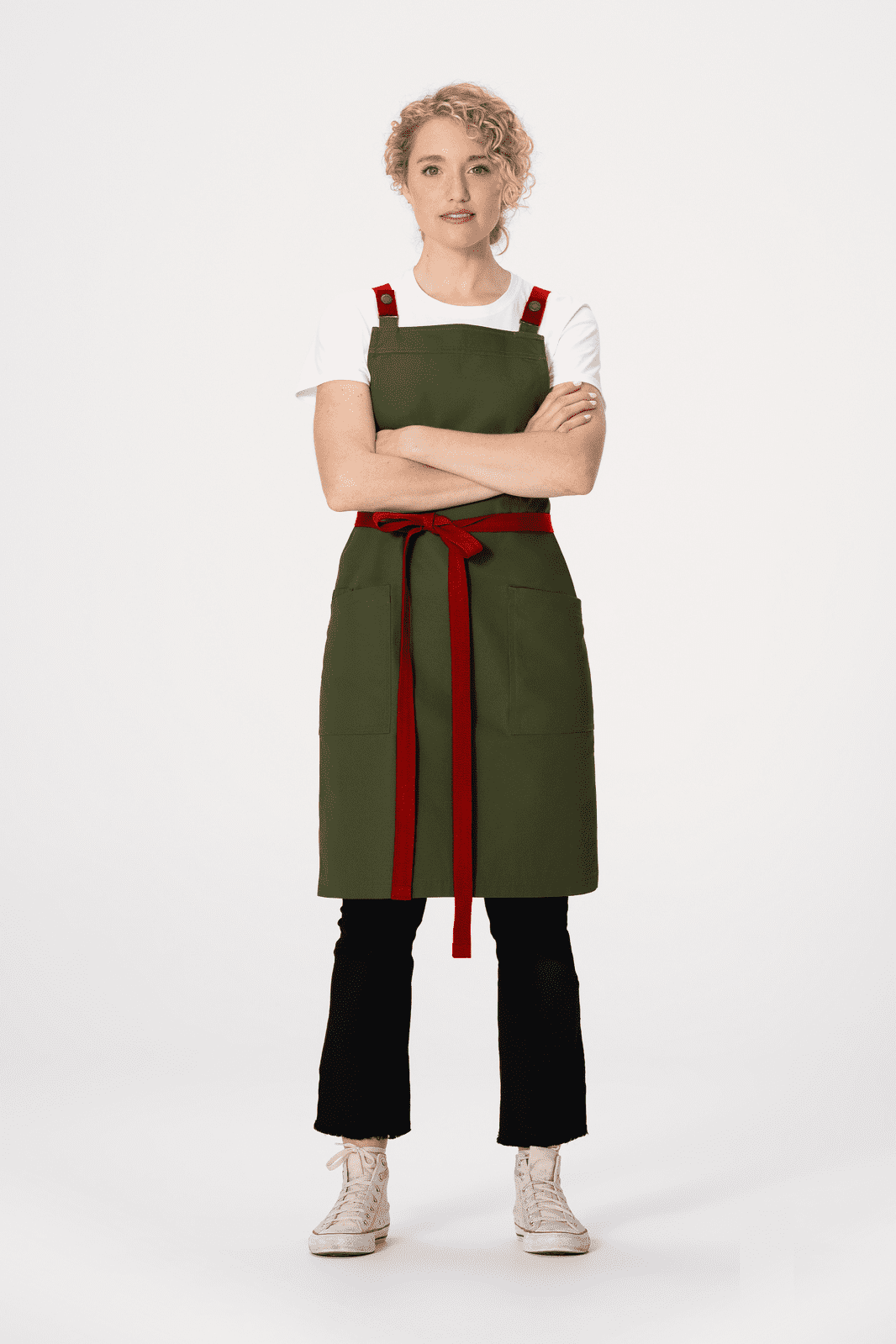A green Lockharte cross back apron with red straps, styled with a white t-shirt and black pants.