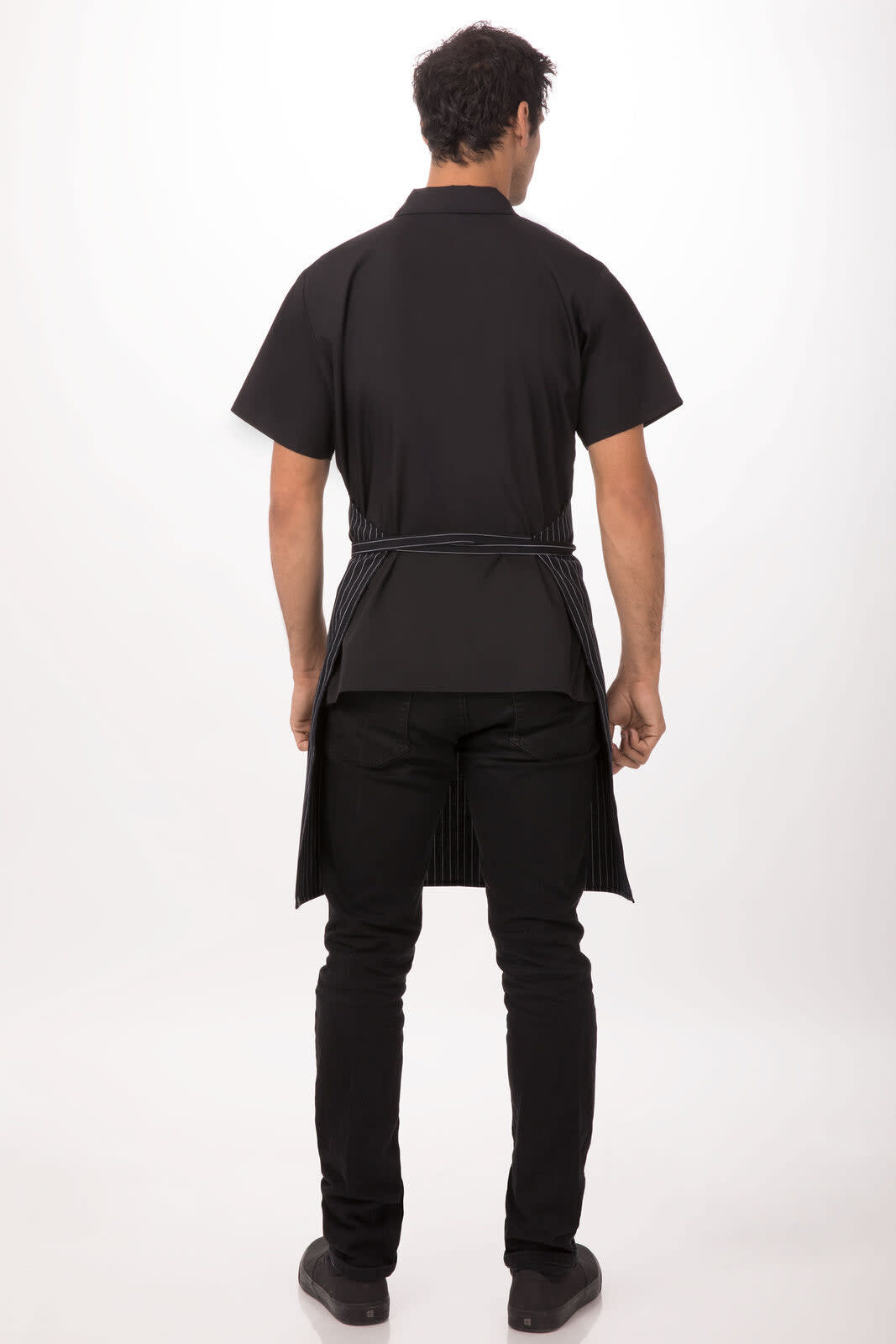 A black adjustable bib apron worn backwards, featuring a secured tie at the waist, displayed on a model.