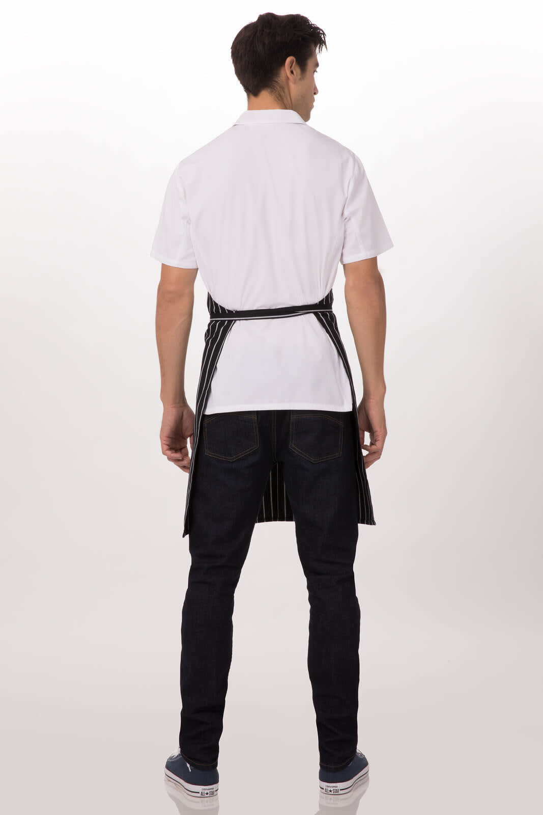 A bib apron in black with white stripes, worn by a person facing away, paired with a white shirt and dark jeans.