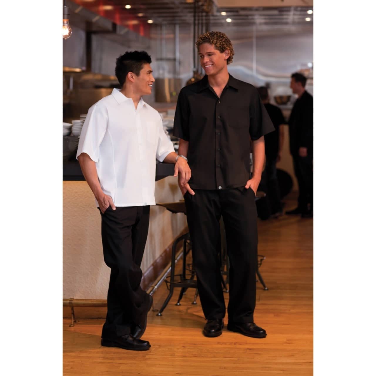 Two men wearing short-sleeved cook shirts, one in white and the other in black, standing in a restaurant setting.