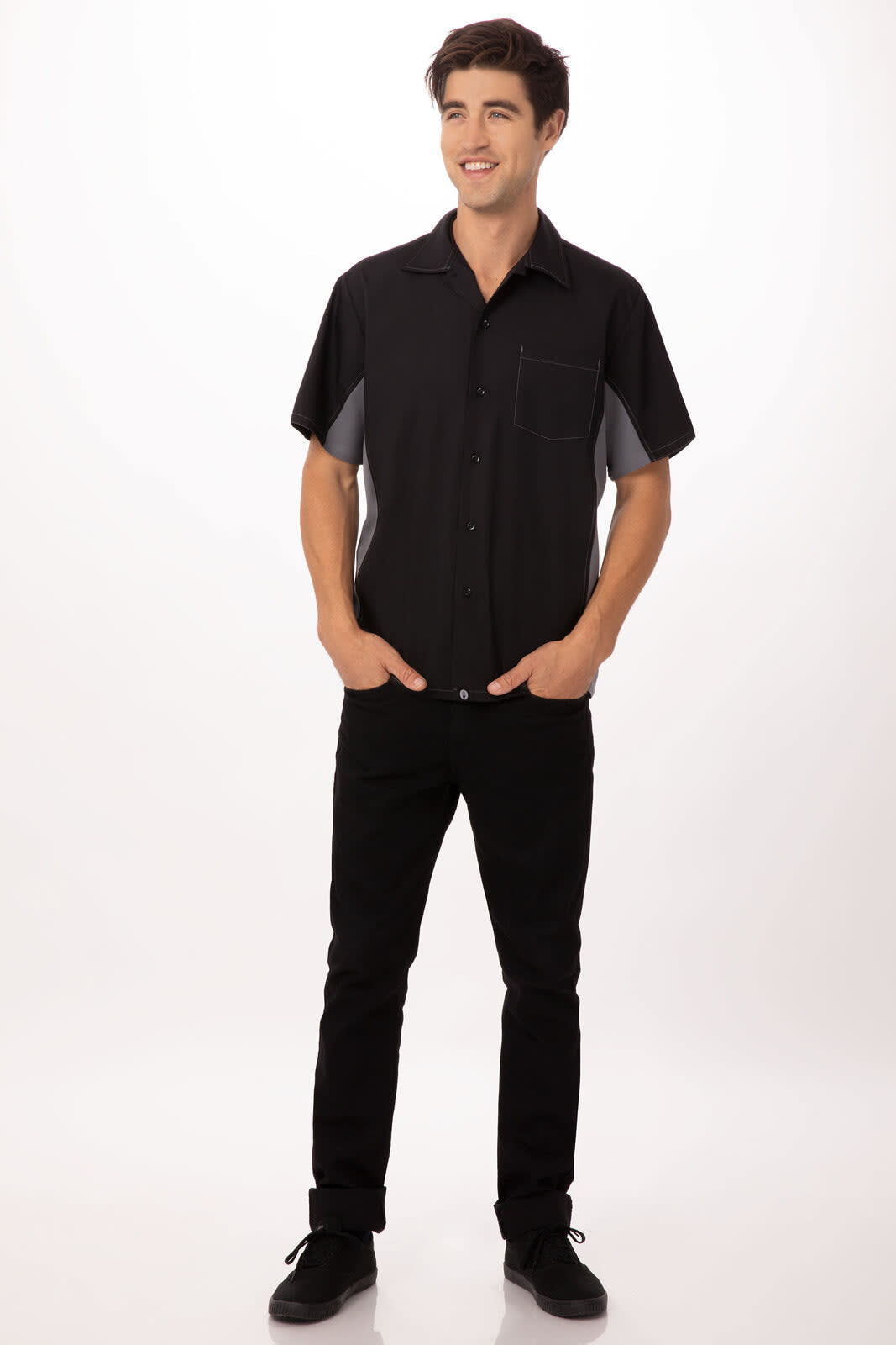 A man wearing a black and grey short-sleeve shirt with a pocket, paired with dark trousers and shoes.
