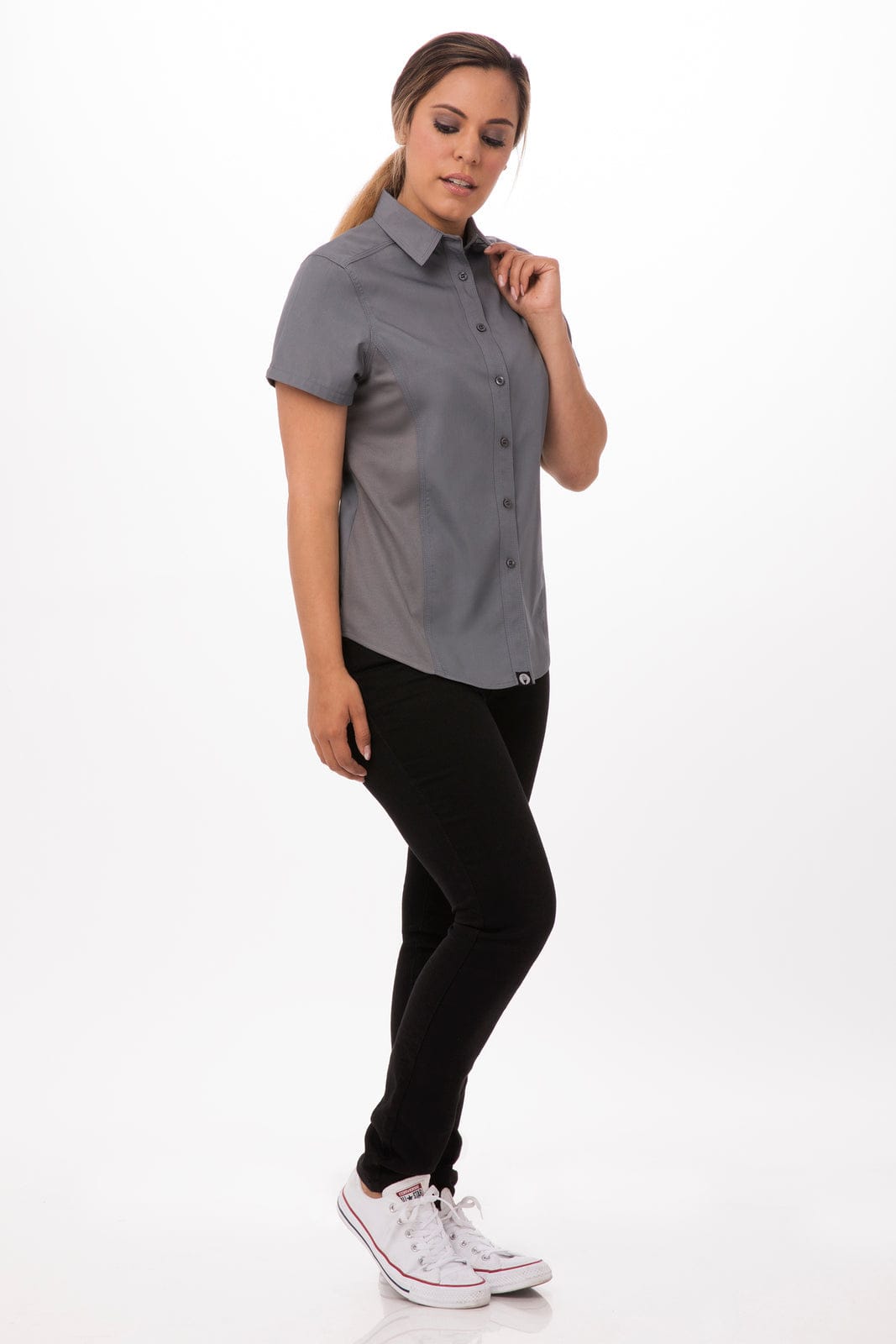 A woman in a grey short-sleeve shirt paired with black pants, standing against a white background. The shirt features a logo.
