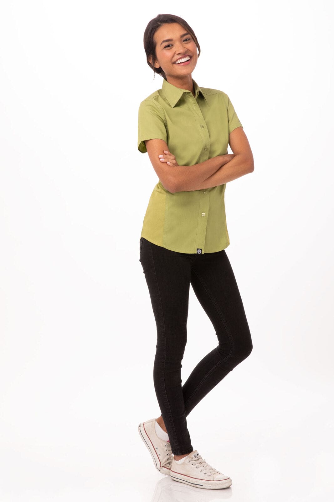A short-sleeved, olive green women's shirt is displayed on a smiling model, paired with black pants and white sneakers.