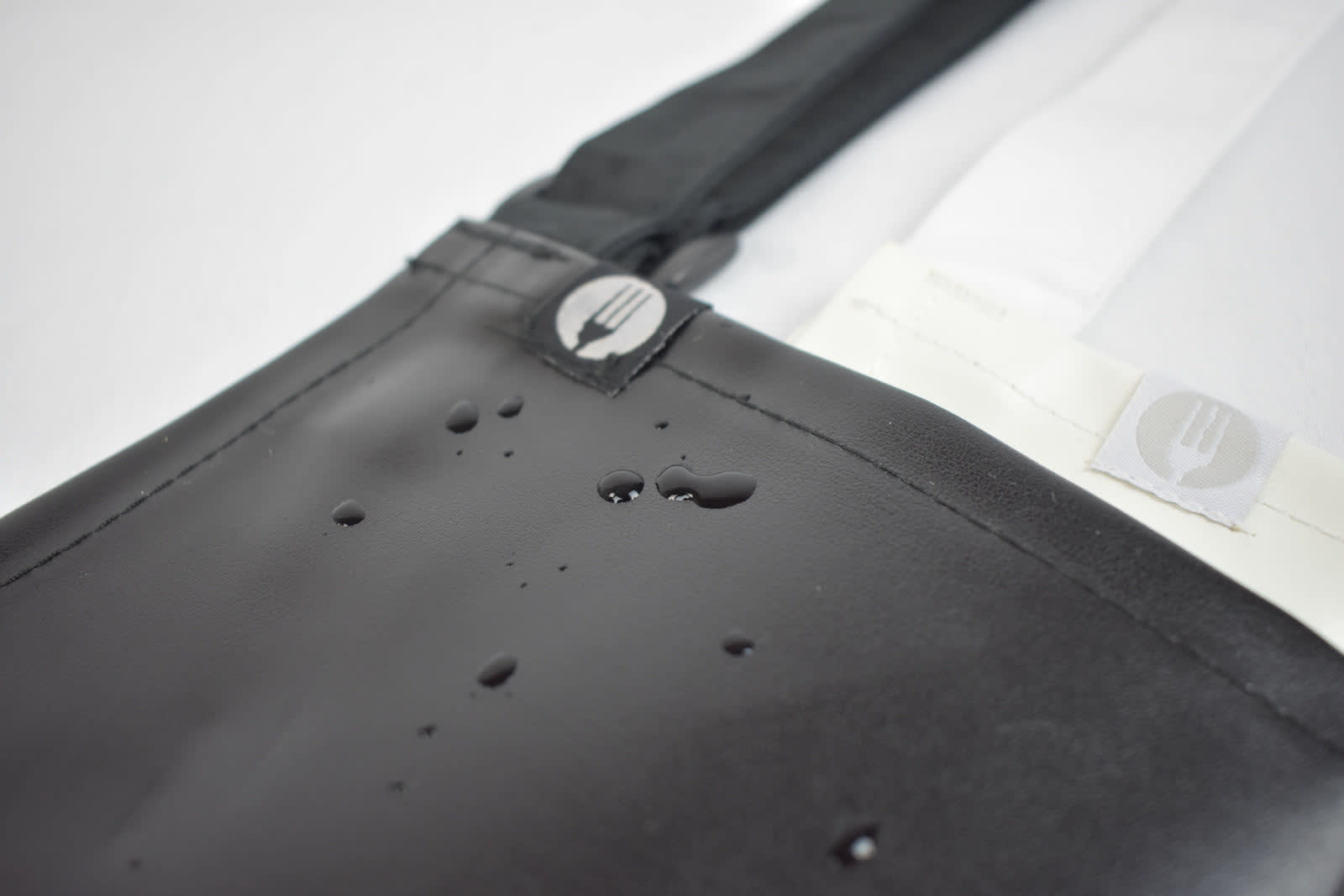 A black PVC bib apron with water droplets, featuring a logo on the strap.