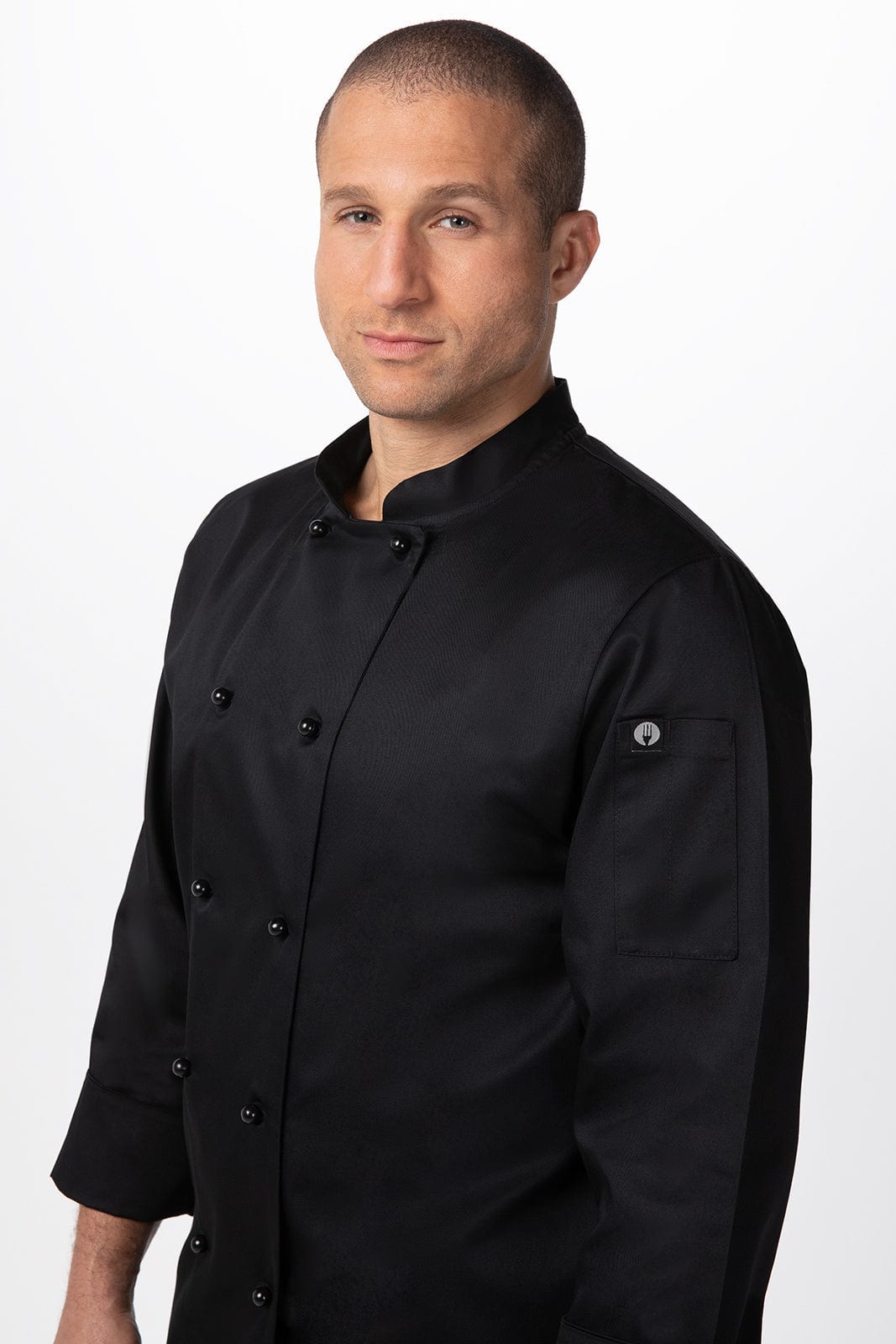 A man wearing a black chef jacket with a logo on the sleeve, posing against a plain background.