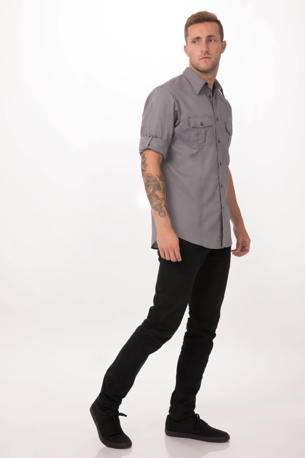 A grey button-up shirt with rolled sleeves, featuring pockets, worn by a model with black jeans and shoes.