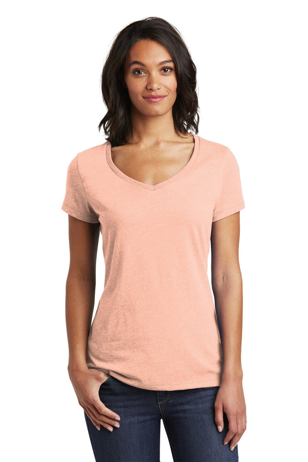 A woman in a peach V-neck t-shirt, standing casually with hands on hips, featuring a logo on the shirt.