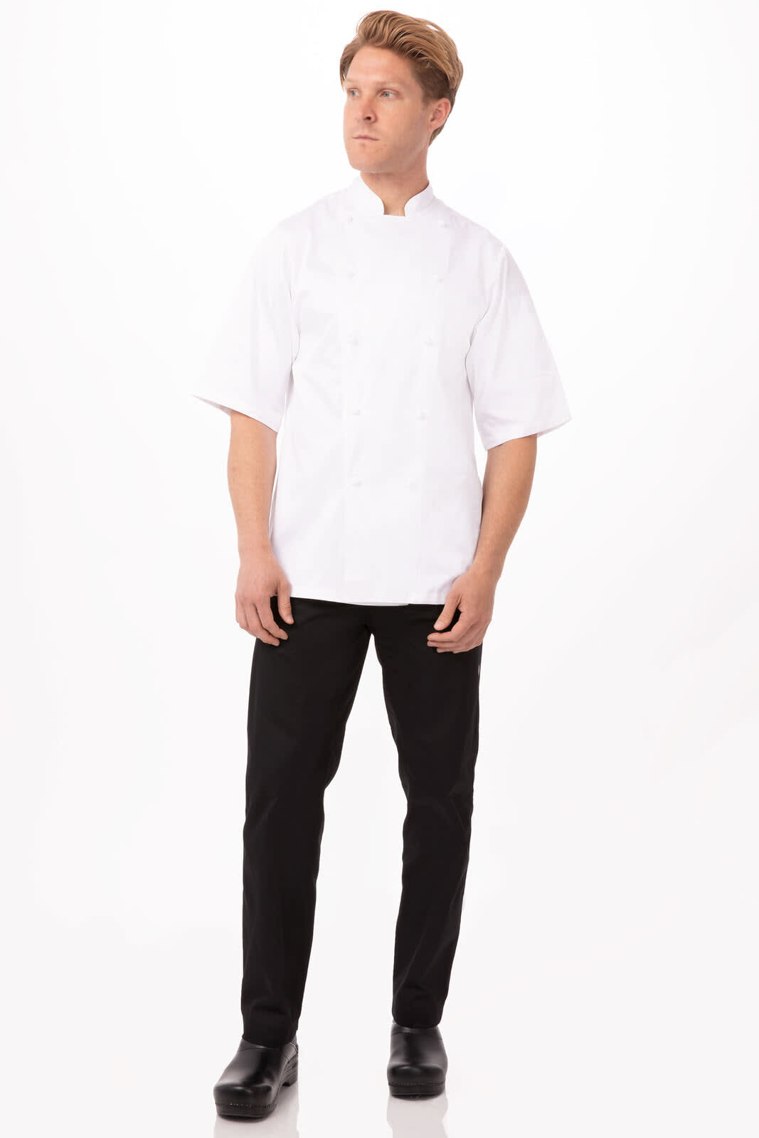A chef in a white Capri Premium Cotton Chef Jacket stands in black trousers and shoes against a plain background.
