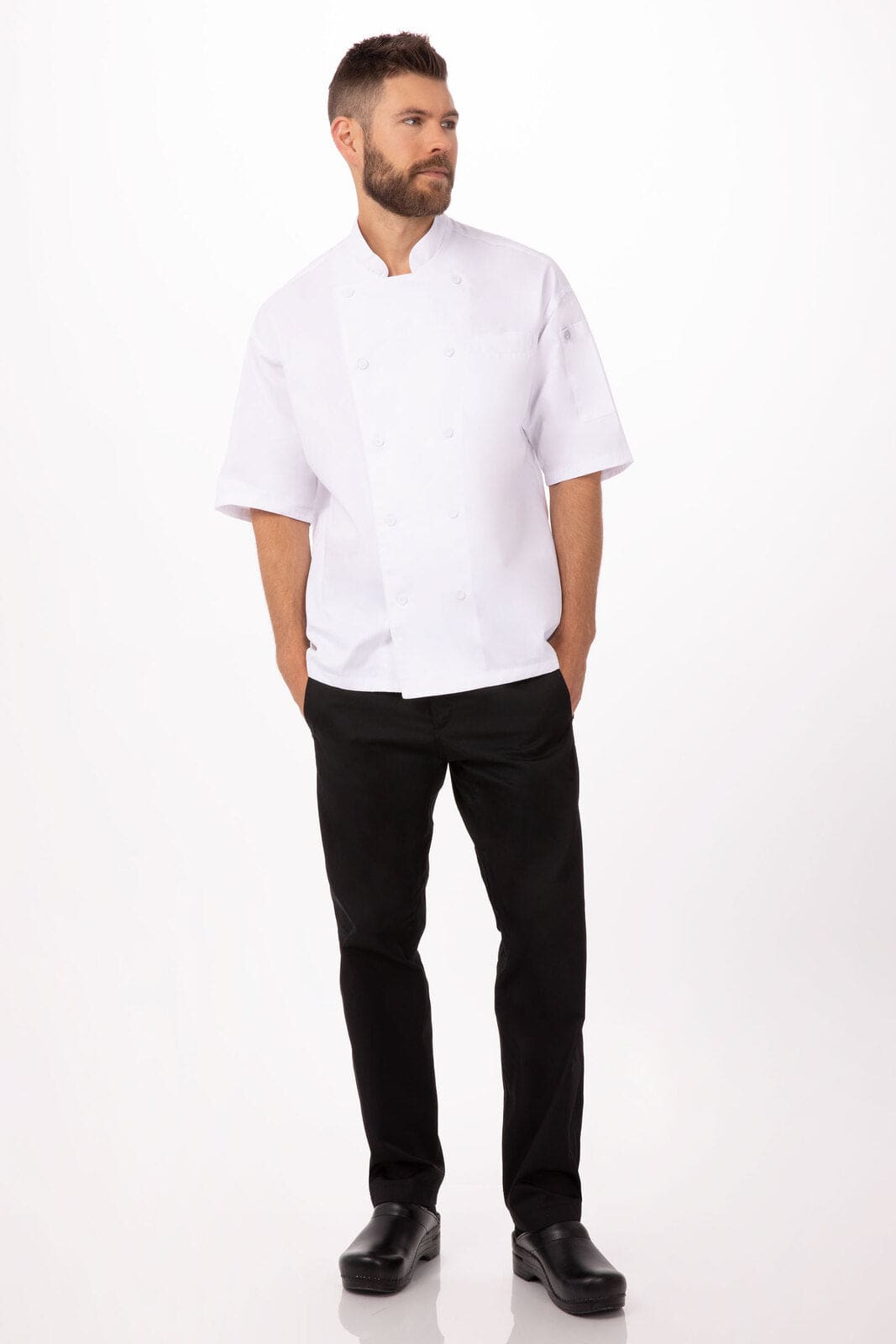A man wearing a white chef jacket and black pants stands against a plain background. The jacket has a logo.