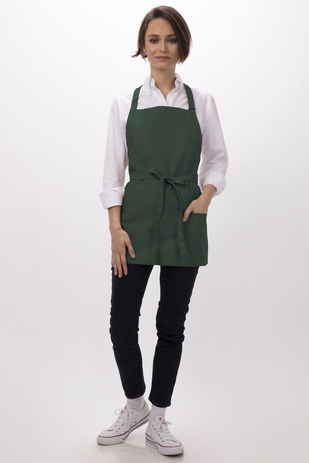 A woman wearing a green apron with three pockets, paired with a white shirt and dark pants.