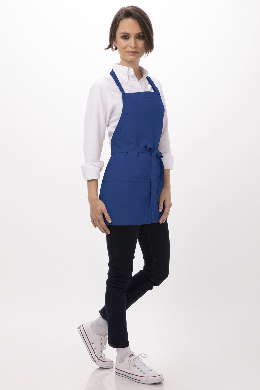 A blue three-pocket apron is worn by a person standing, styled with a white shirt and dark trousers. The apron features a logo.