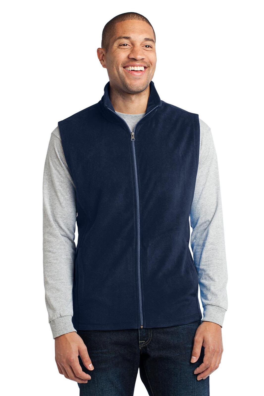A navy microfleece vest is worn over a grey long-sleeve top by a smiling man. The vest features a front zipper.