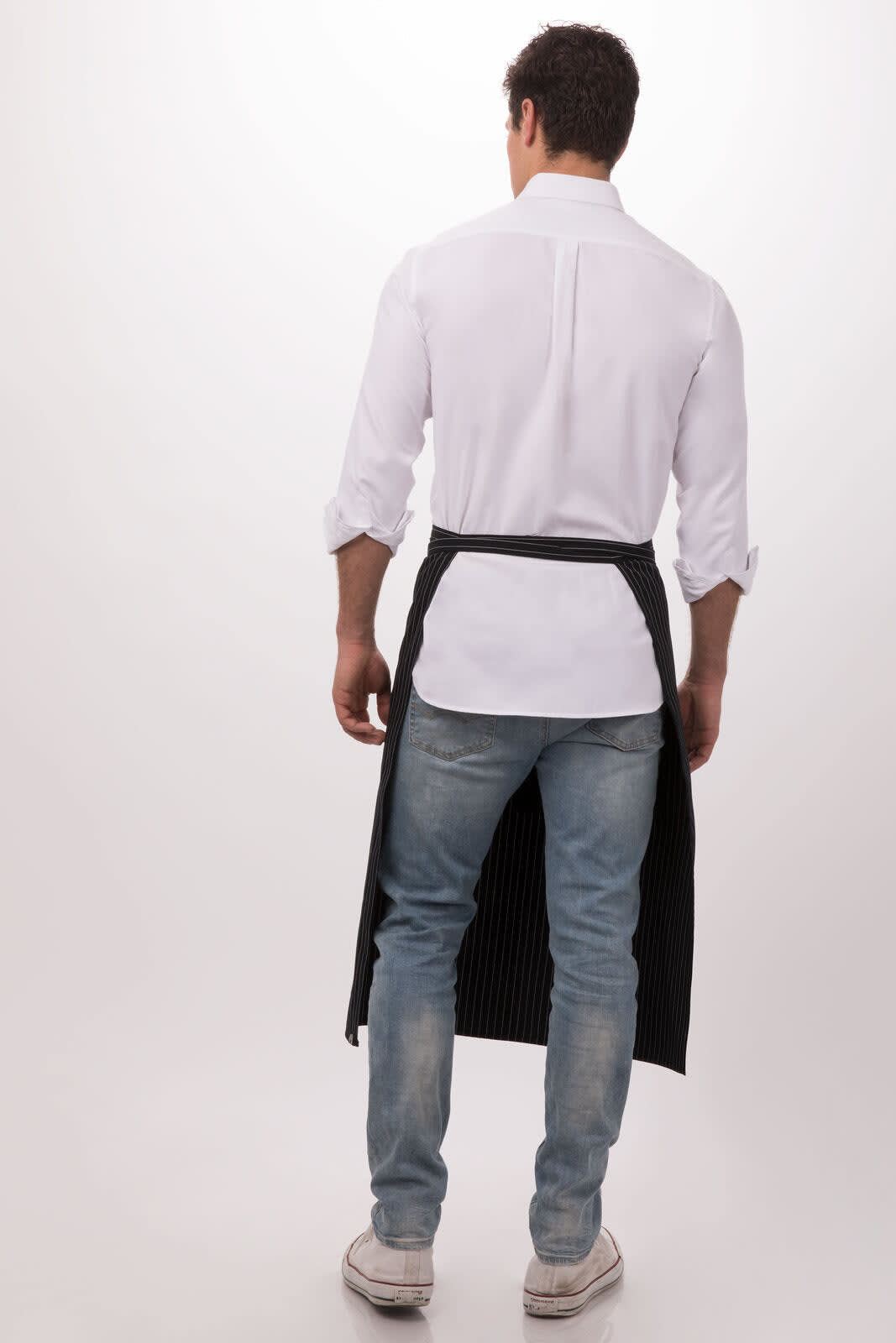 A man stands with his back to the camera, wearing a black and white striped Bistro apron over casual jeans and a white shirt.