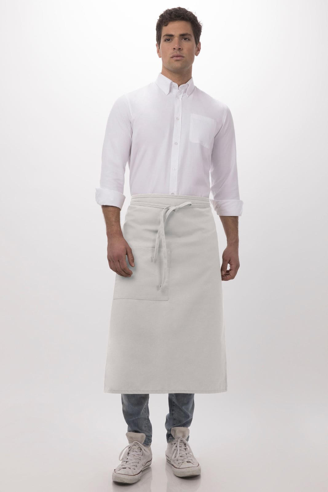 A man in a white shirt and grey bistro apron stands against a plain background. The apron features a tie and a logo.