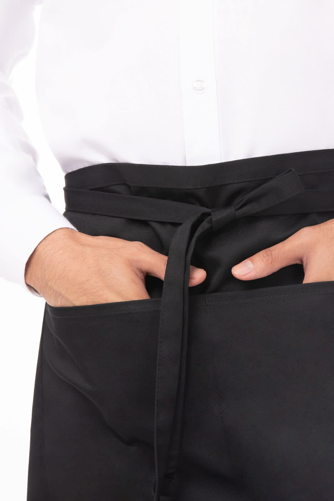 A black half bistro apron with a person’s hands in the front pockets, worn over a white shirt.