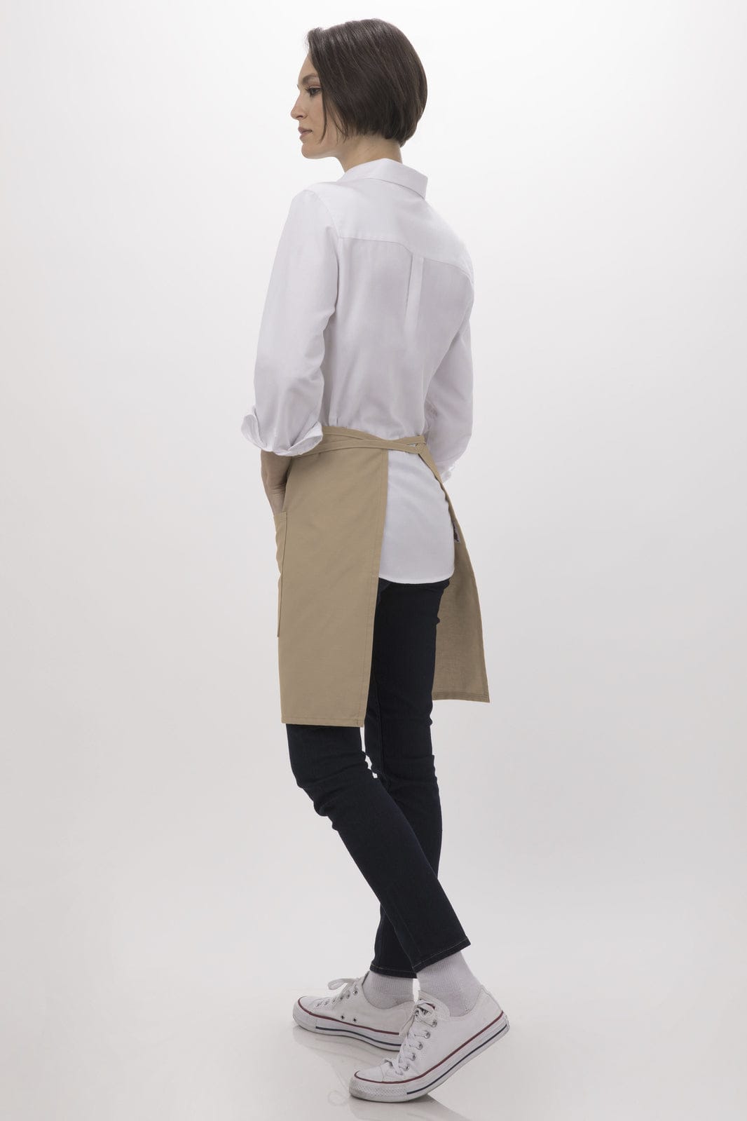 A half bistro apron in beige, worn over a white shirt and black pants, with a model standing sideways.