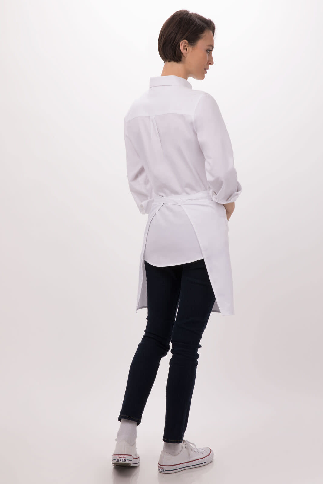 A white half bistro apron worn over dark jeans, with a button-up shirt, featuring a back sash and a logo.