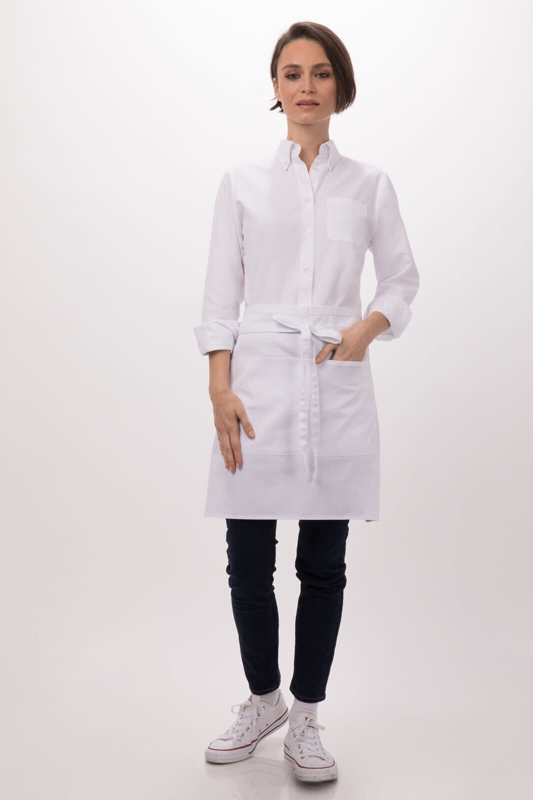 A white half bistro apron worn over a button-up shirt, paired with dark pants and white sneakers. The apron features a logo.