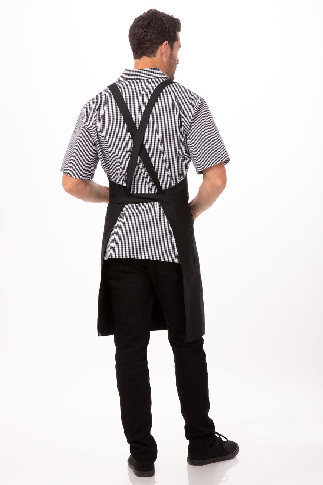 A black cross-back bib apron worn over a checked shirt, showcased from the back on a model.