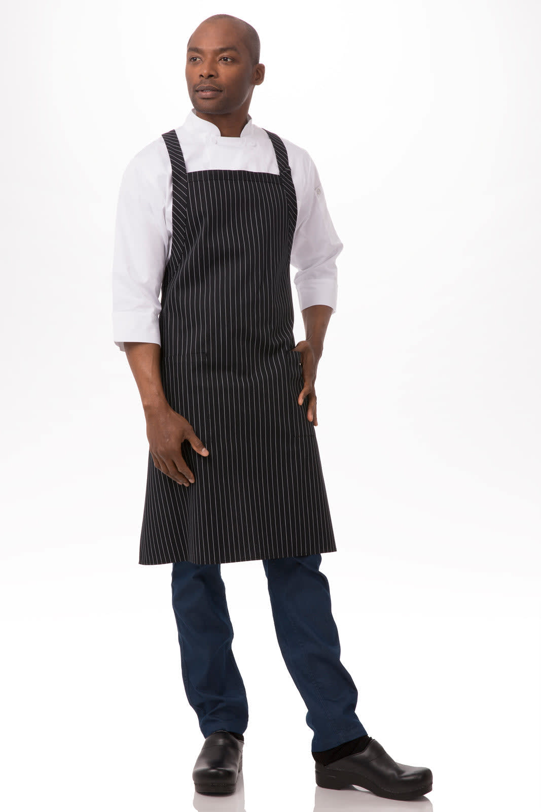 A black and white striped cross-back bib apron worn by a model, paired with a white shirt and dark trousers.