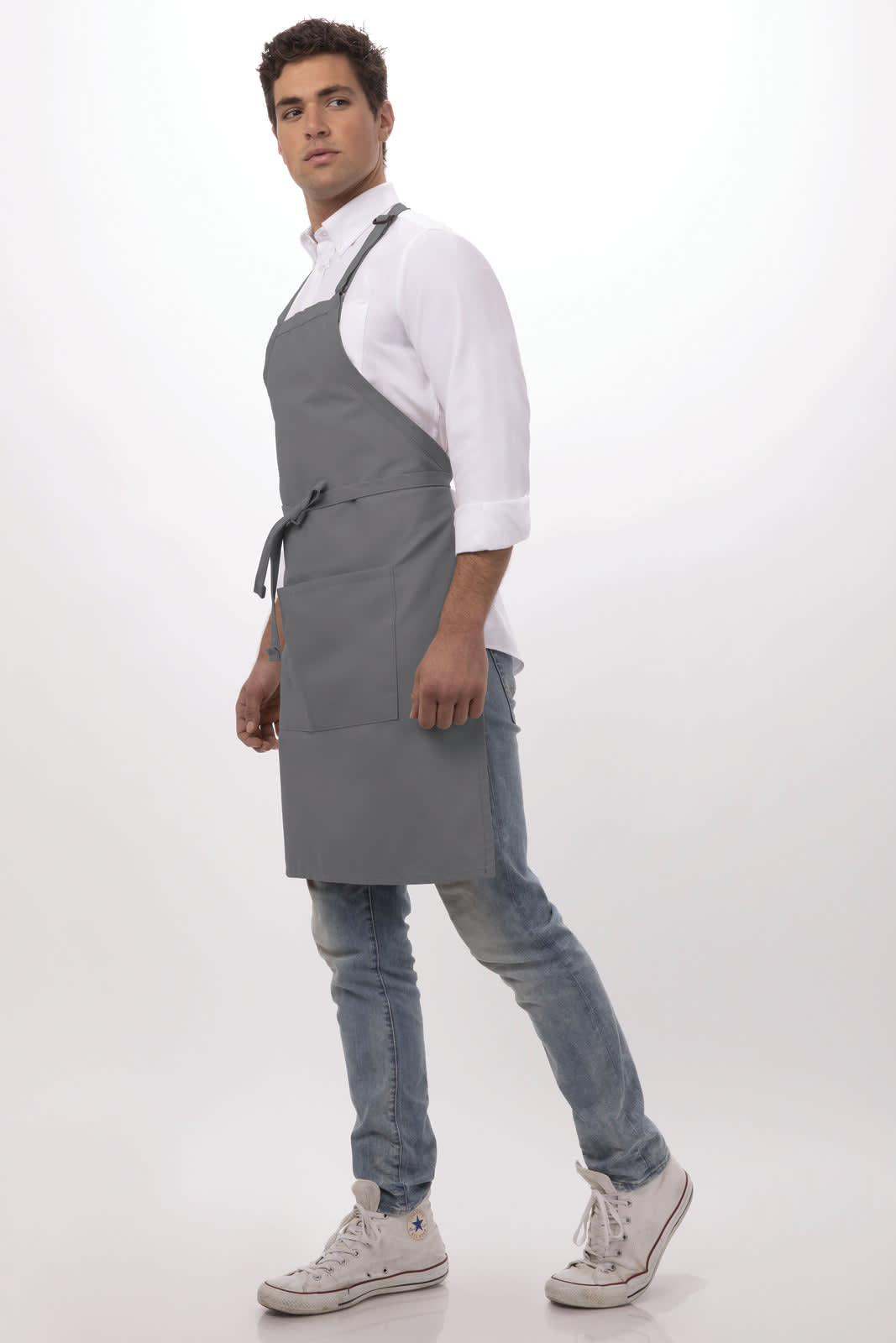 A grey bib apron is worn by a model standing against a neutral background. The apron has a logo and a tie waist.