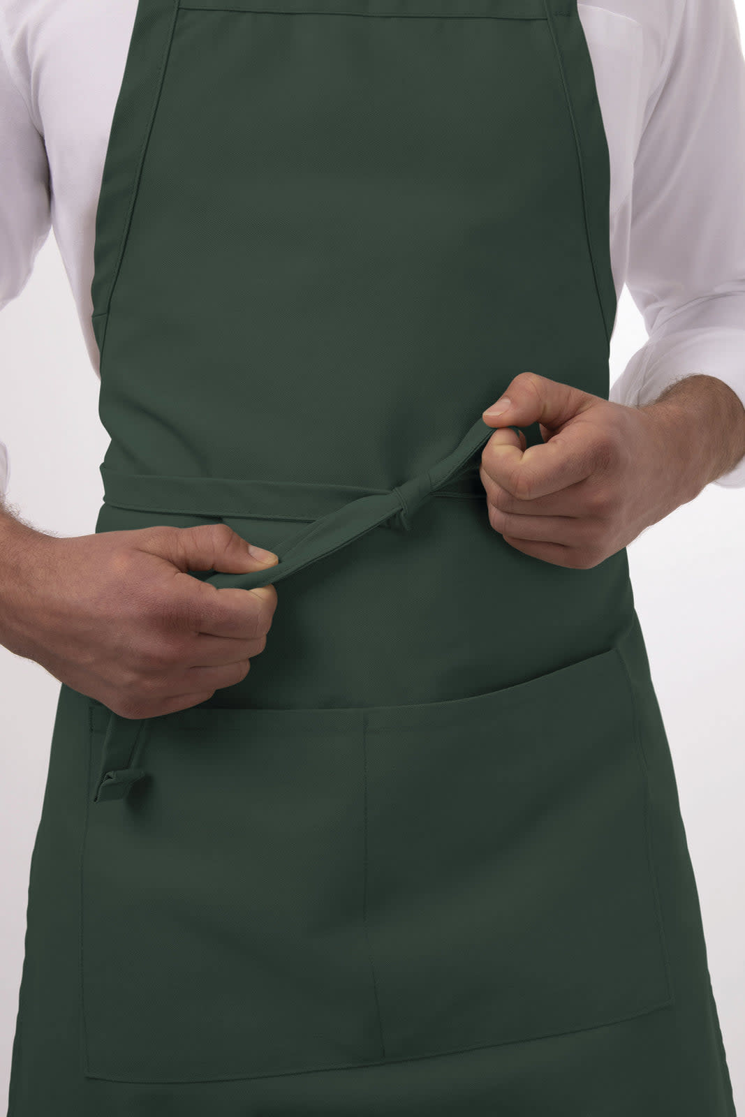 A dark green bib apron is being adjusted, featuring a front pocket and a secure tie at the waist.