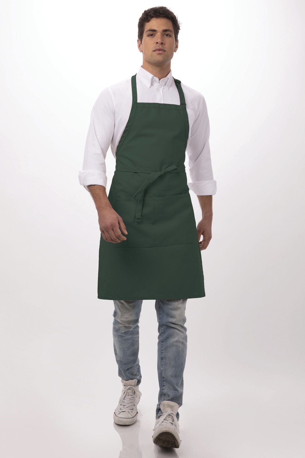 A green bib apron worn by a model, featuring adjustable straps and a front pocket. The model is styled casually.