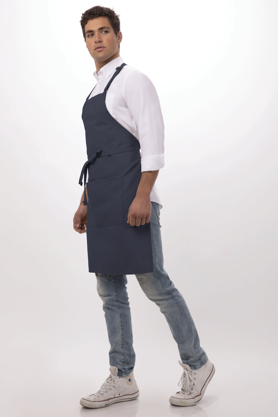 A navy bib apron worn by a model, featuring ties and a logo, paired with a white shirt and jeans.