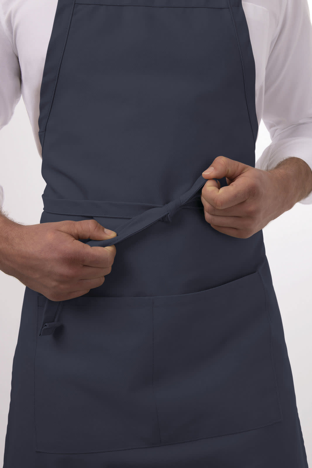 A navy blue bib apron features a front pocket and is being adjusted by a person. It has a logo on it.