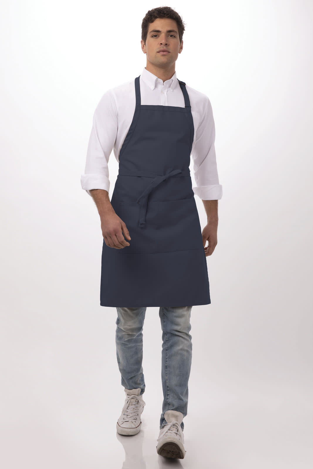 A navy bib apron worn by a person with a white shirt and jeans, featuring a logo.