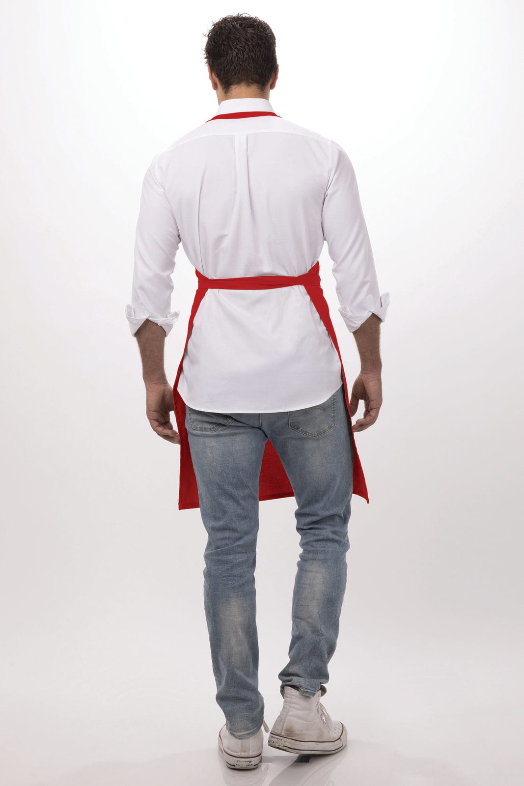 A person wearing a white shirt and blue jeans, with a red bib apron tied at the back. The apron has a logo.