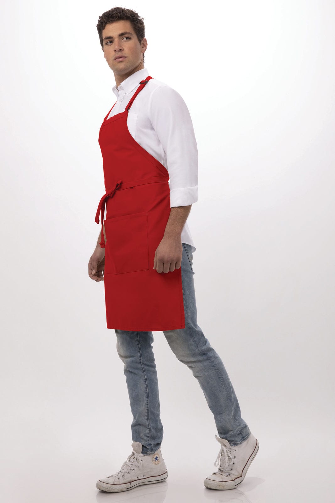 A red bib apron is worn by a model standing in profile, paired with a white shirt and jeans.