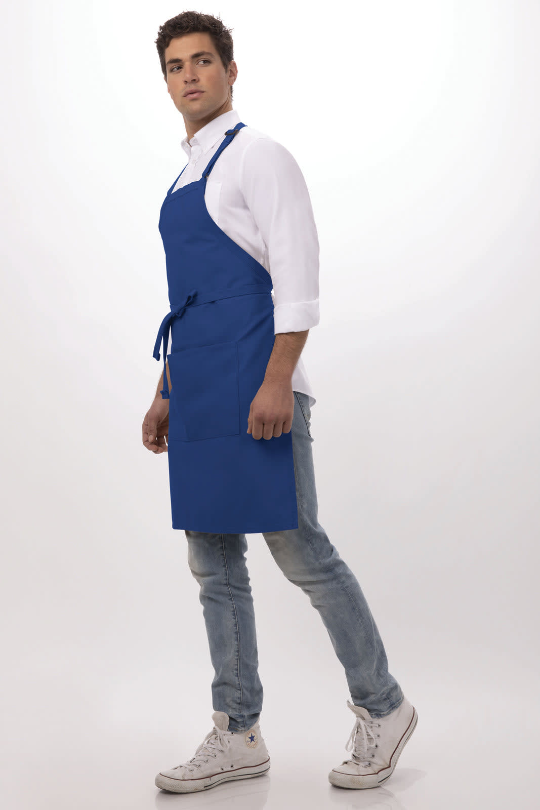 A blue bib apron worn by a model standing sideways, featuring ties at the waist and a logo on the apron.