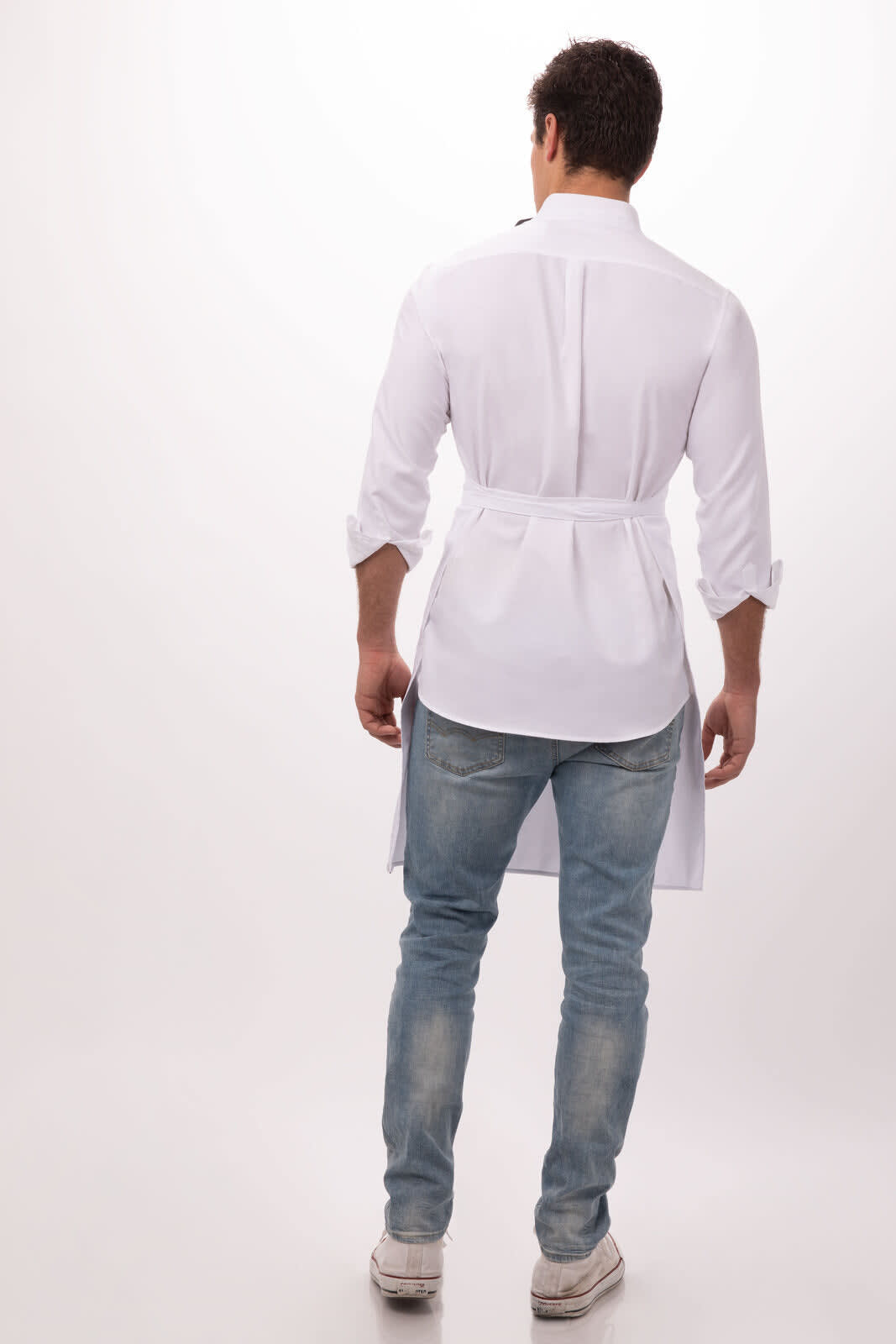 A white bib apron worn by a model, featuring long sleeves and a waist tie, paired with light blue jeans.