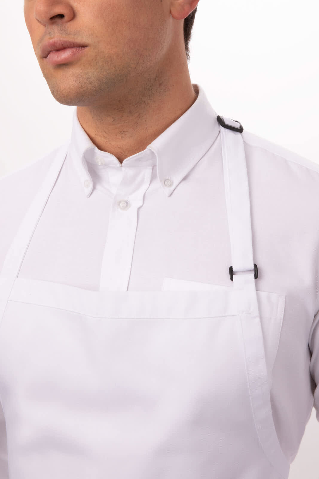 A white bib apron with adjustable straps, worn by a person in a button-up shirt. The apron features a pocket.