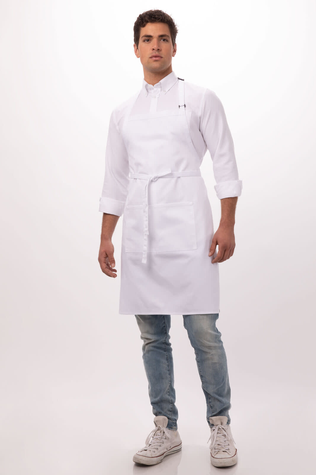A white bib apron worn by a model, paired with a collared shirt, denim jeans, and sneakers. The apron features a logo.