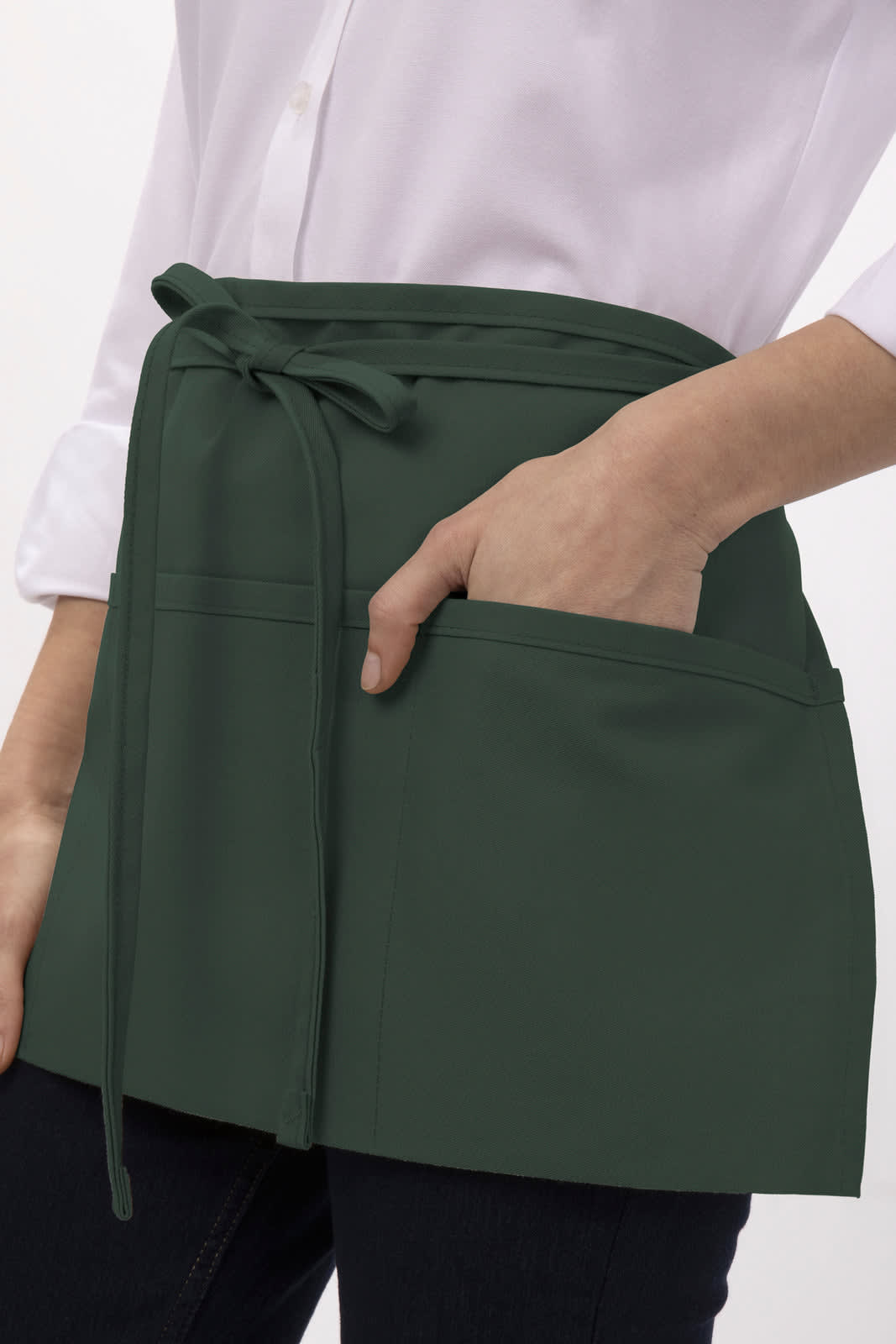 A dark green waist apron with a tie waist and front pockets, worn by a person in a white shirt.