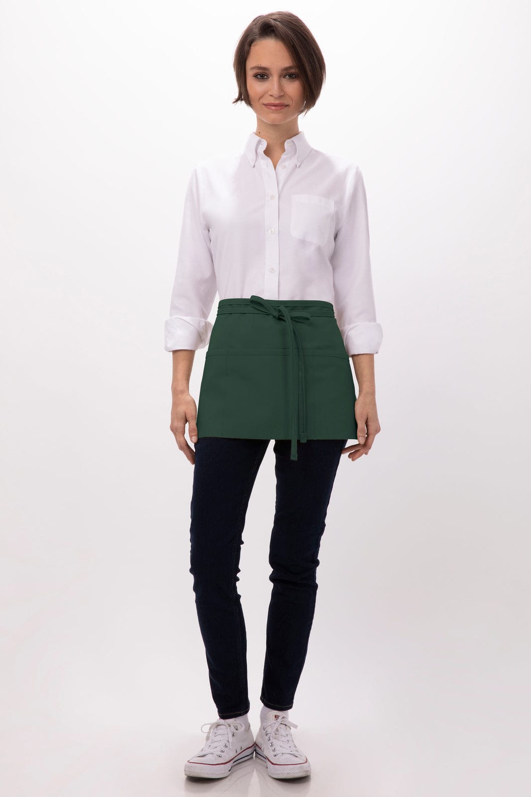 A woman wearing a white shirt and a green waist apron, standing against a plain background. The apron has a tie at the waist.
