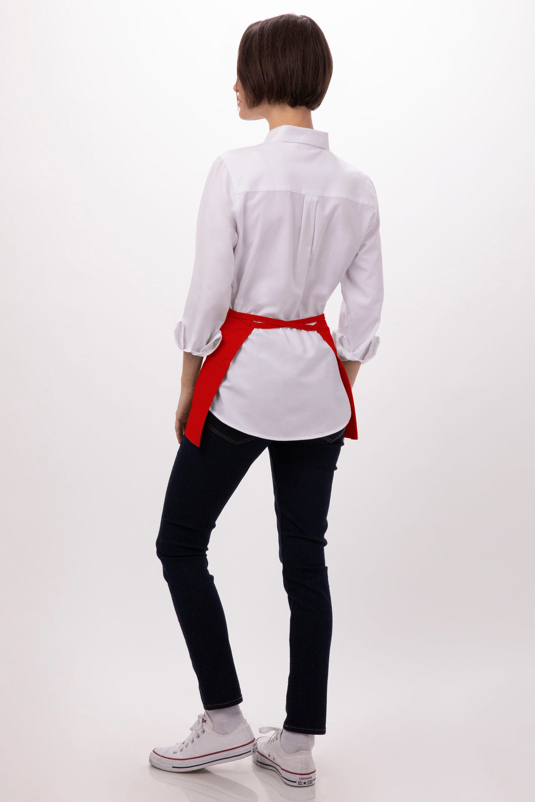 A waist apron in red worn over a white shirt, paired with black jeans and white shoes, displaying a logo.
