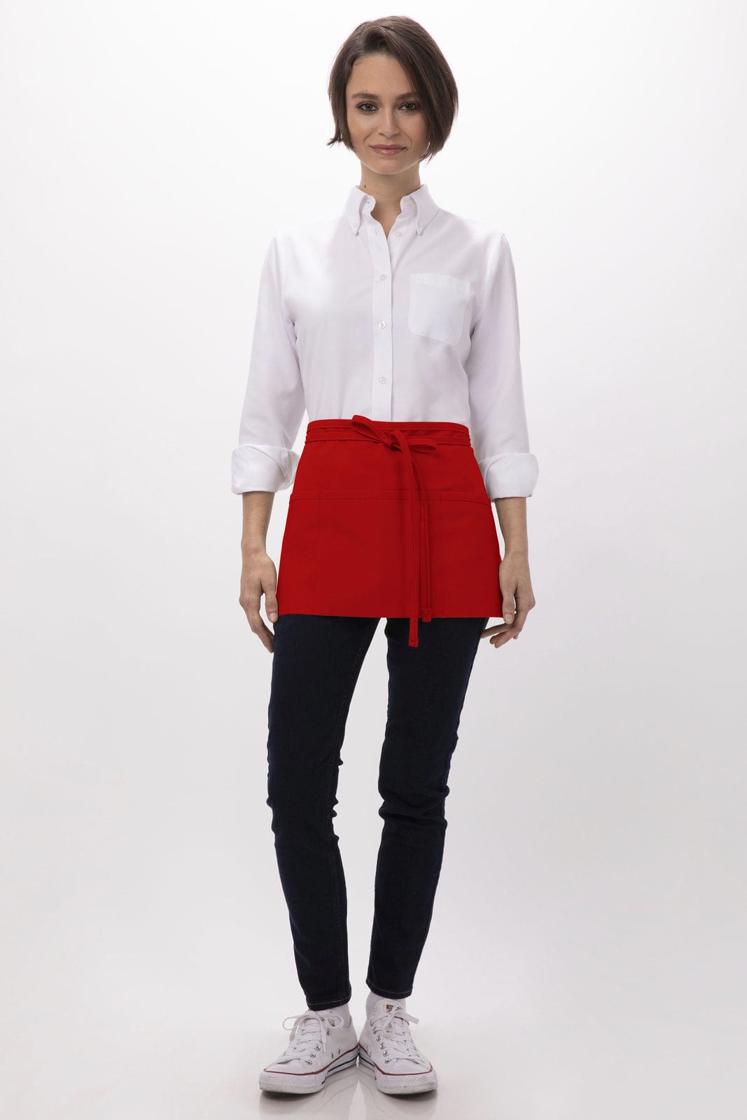A woman in a white shirt and black pants wears a red waist apron with a tied belt, standing against a neutral background.