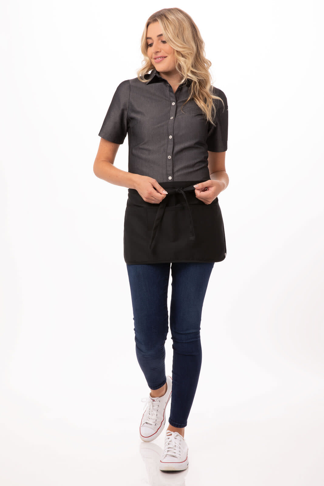 A woman models a reversible waist apron in black, paired with a grey shirt and blue jeans, featuring a logo.