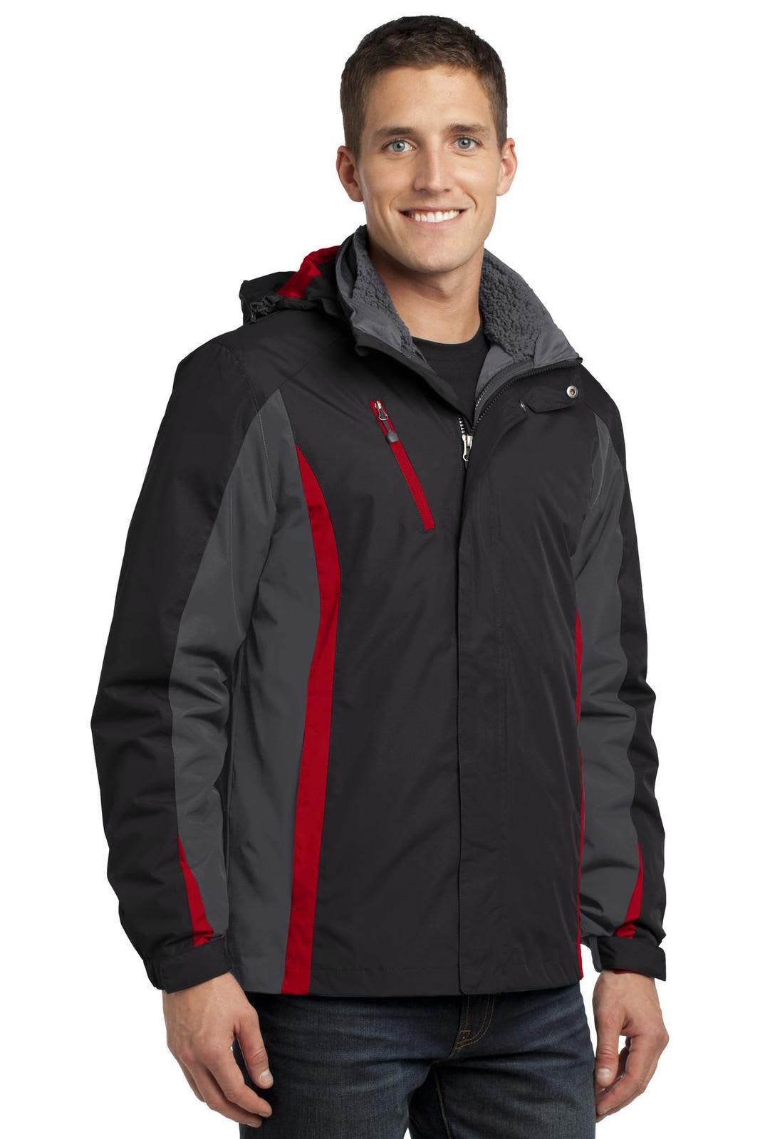 A man wearing a black and grey jacket with red accents, featuring a hood and zippered pockets, stands smiling.