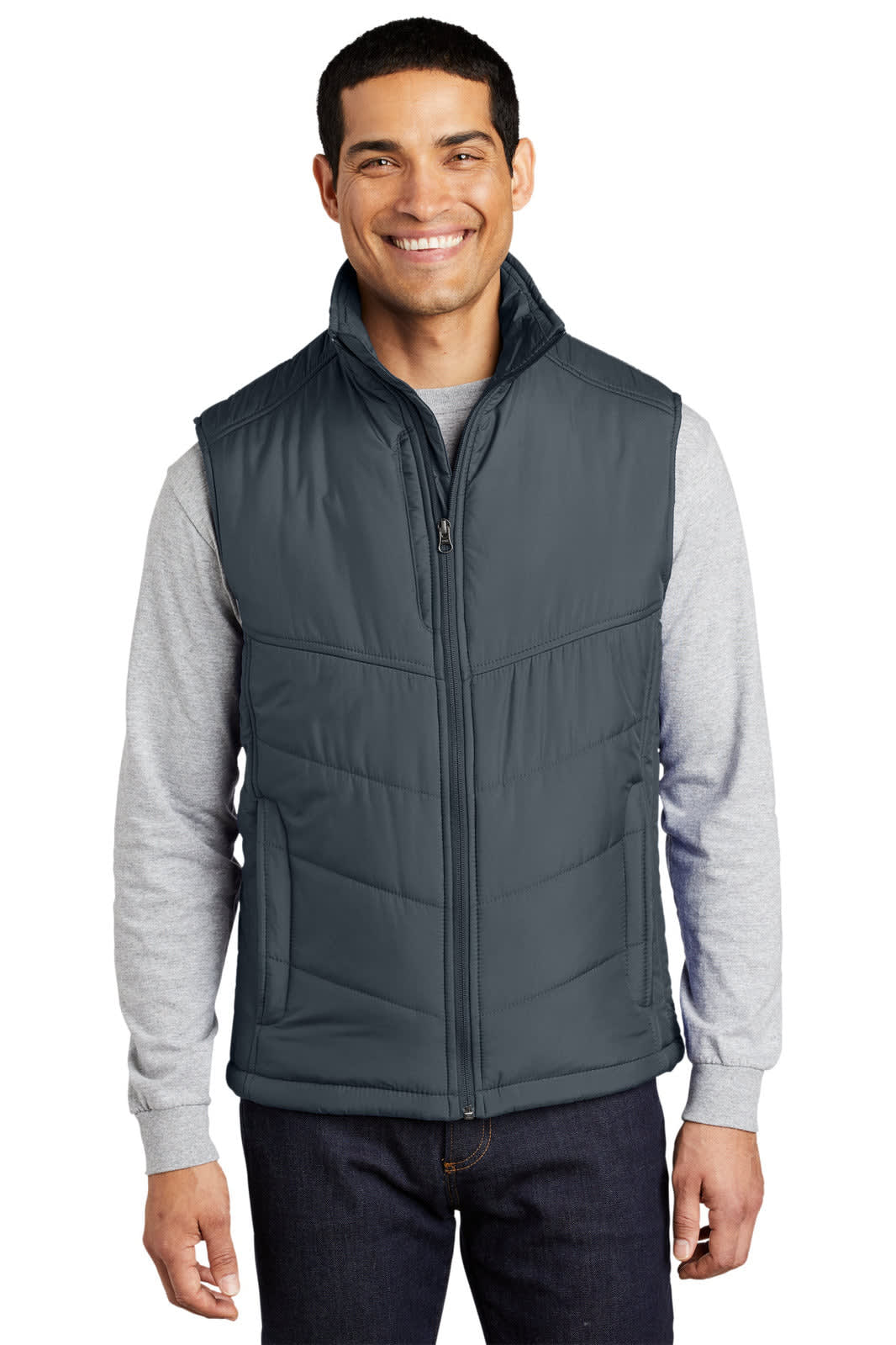 A man wearing a grey puffy vest over a light grey long-sleeve shirt and dark jeans, smiling at the camera.