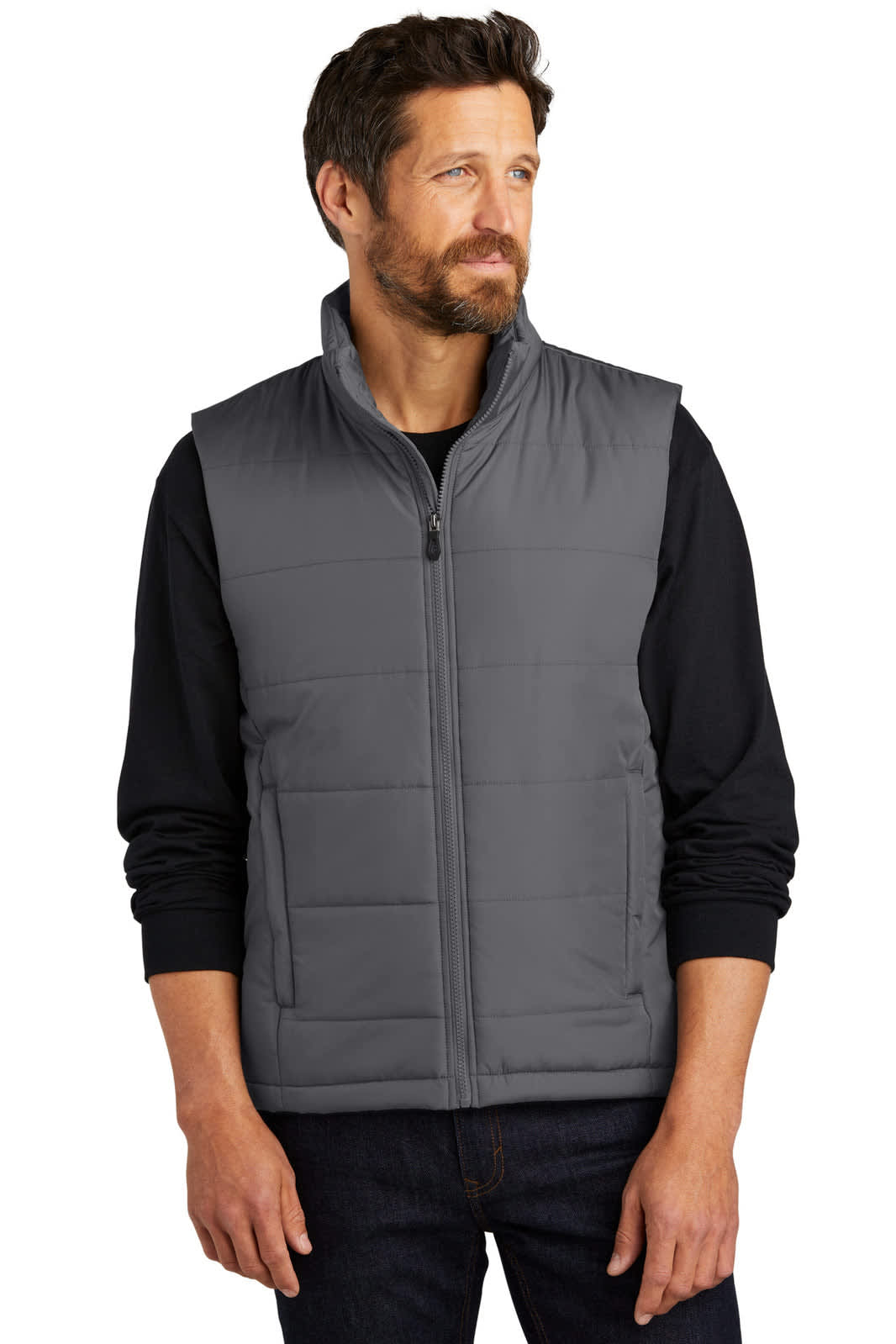 A man is wearing a grey puffer vest over a black long-sleeve shirt, standing with a neutral expression.