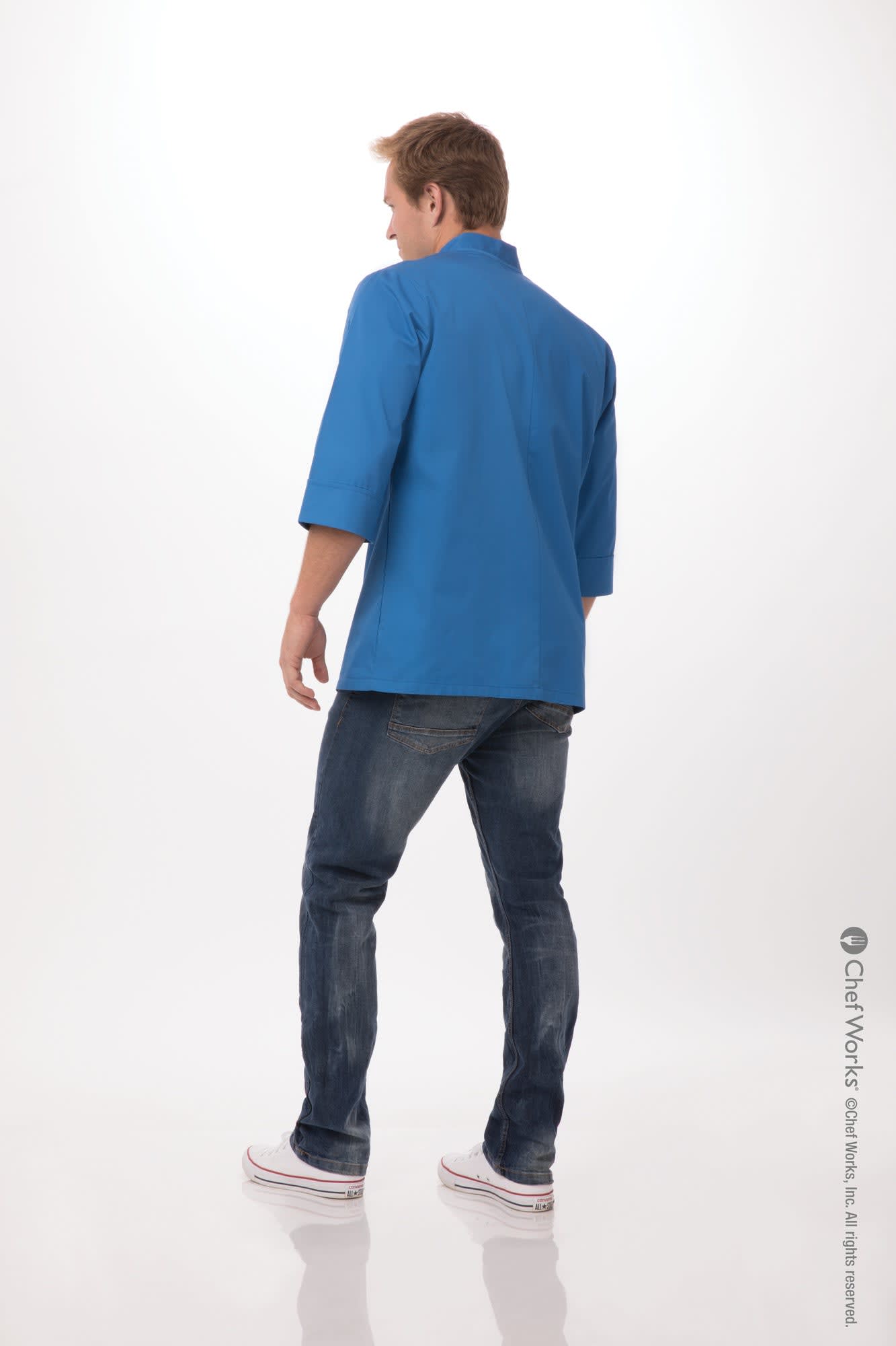 A blue chef jacket viewed from the back, paired with jeans and sneakers, featuring a branding logo.